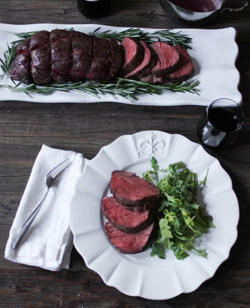 Dinner table with platter of sliced beef tenderloin and a plated serving with salad and red wine.
