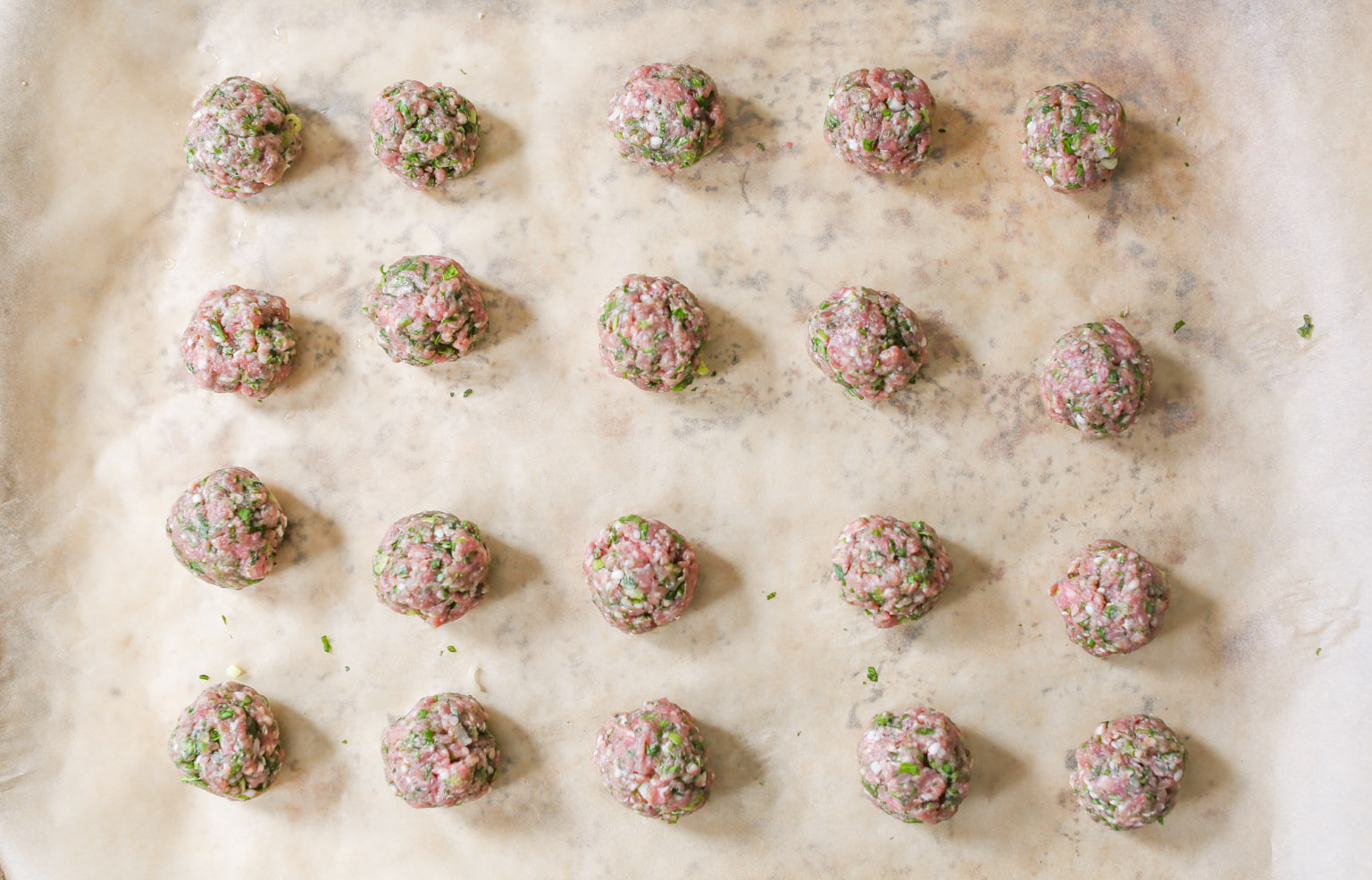 Rolled spiced lamb meatballs on a parchment-lined baking sheet before going into the oven.